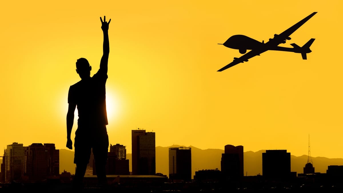 silhouette of student making ASU fork hand sign against city skyline with military drone flying overhead