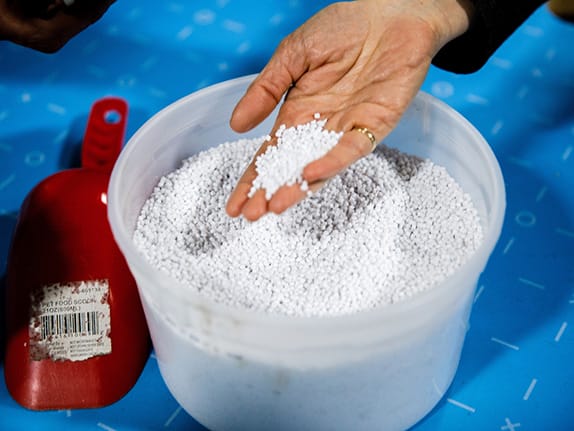 Container of plastic pellets with a person's hand holding some on their fingers.